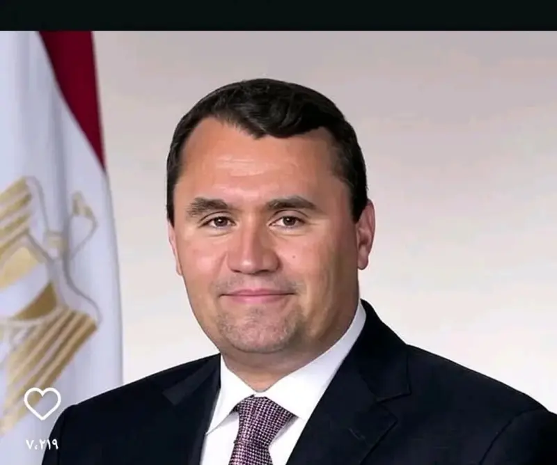 A man in a suit and tie is standing in front of a flag.