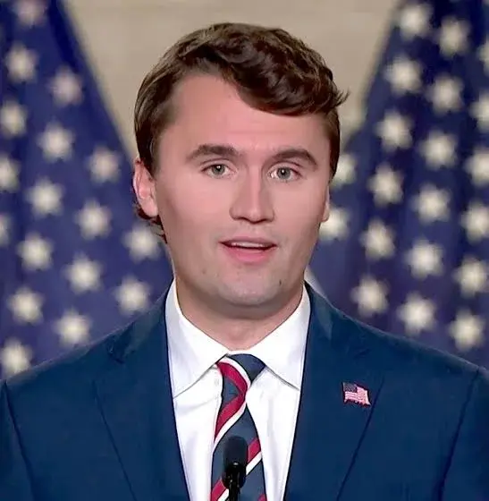 A man in a suit and tie standing in front of an american flag.