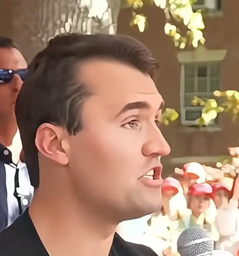 A man in a black shirt and sunglasses speaking into a microphone.