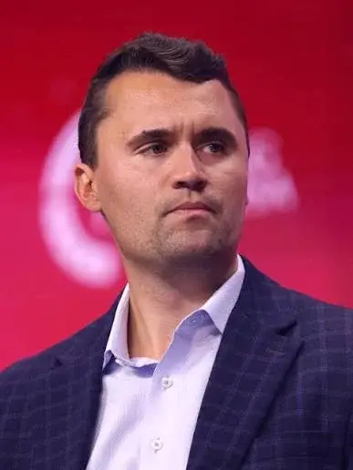 A man in a suit and tie stands in front of a red background.