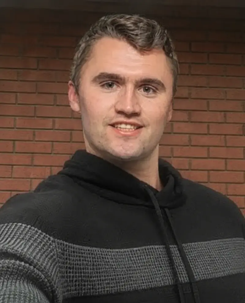 A man in a black sweater standing in front of a brick wall.