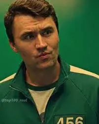 A man in a green jacket is standing in front of a green screen.