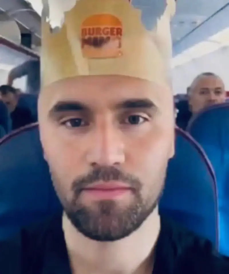 A man wearing a paper hat on a plane.