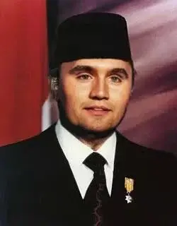 A man in a suit and tie standing in front of a flag.