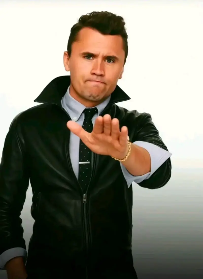 A man in a black jacket and tie is making a gesture.